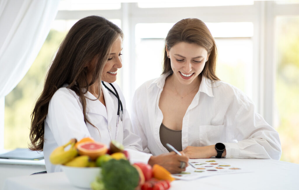 Cheerful adult caucasian nutritionist doctor in white coat makes notes of weight loss plan to young