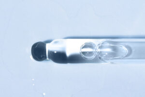 Cosmetic product liquid in a glass dropper on a blue background flat lay. Peptide, serum