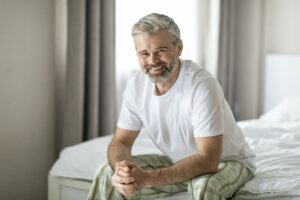 Portrait of happy middle aged man sitting on bed, smiling